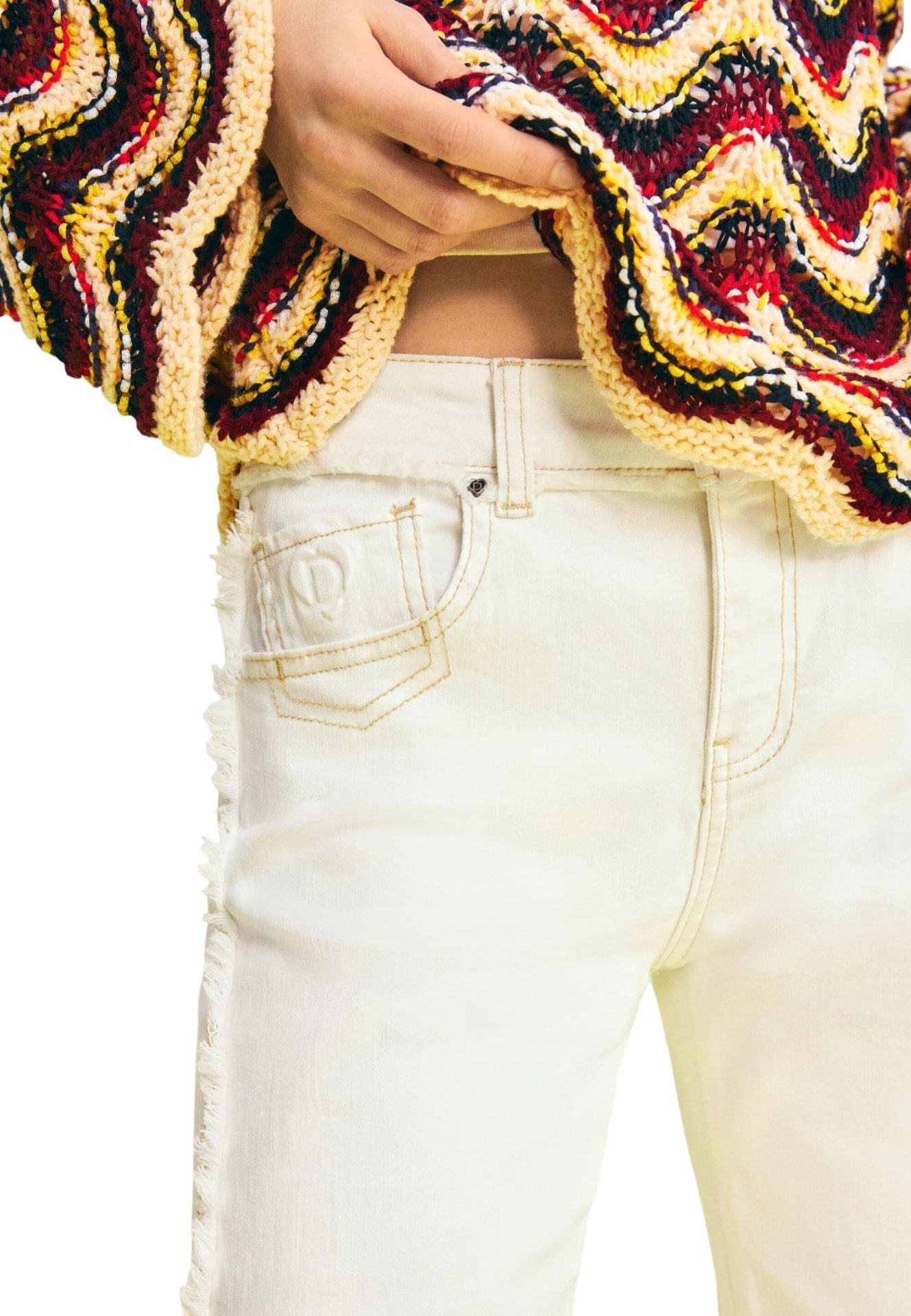 Close-up of high-waisted white jeans with frayed side seams, paired with a colorful wavy-patterned knit sweater