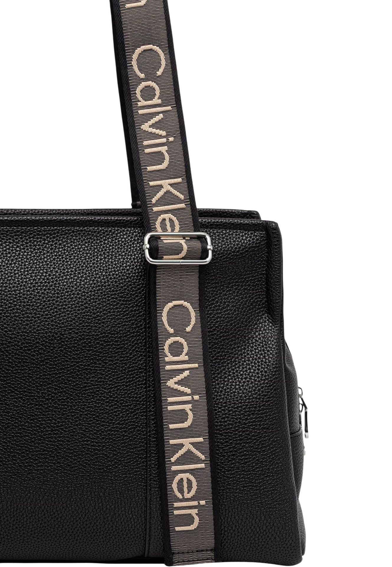 Close-up of a black pebbled leather bag with a beige Calvin Klein branded fabric strap and silver buckle