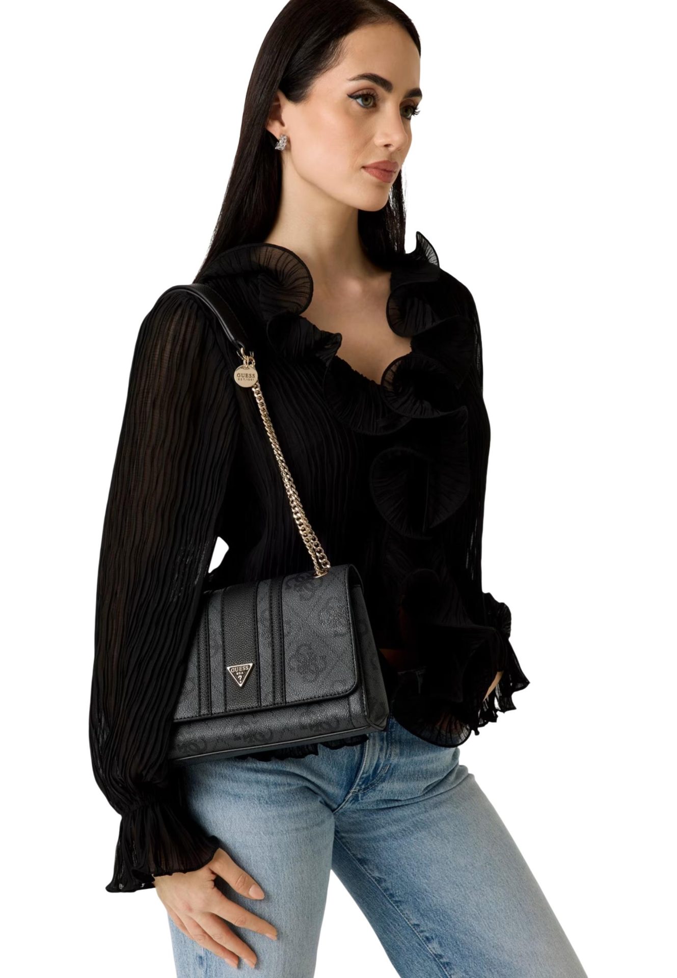 Black Guess shoulder bag with a gold chain strap, worn by a model in a black ruffled blouse and jeans