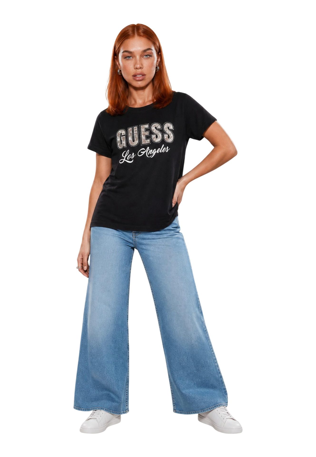 Model wearing a black t-shirt with GUESS Los Angeles logo, wide-leg blue jeans, and white sneakers